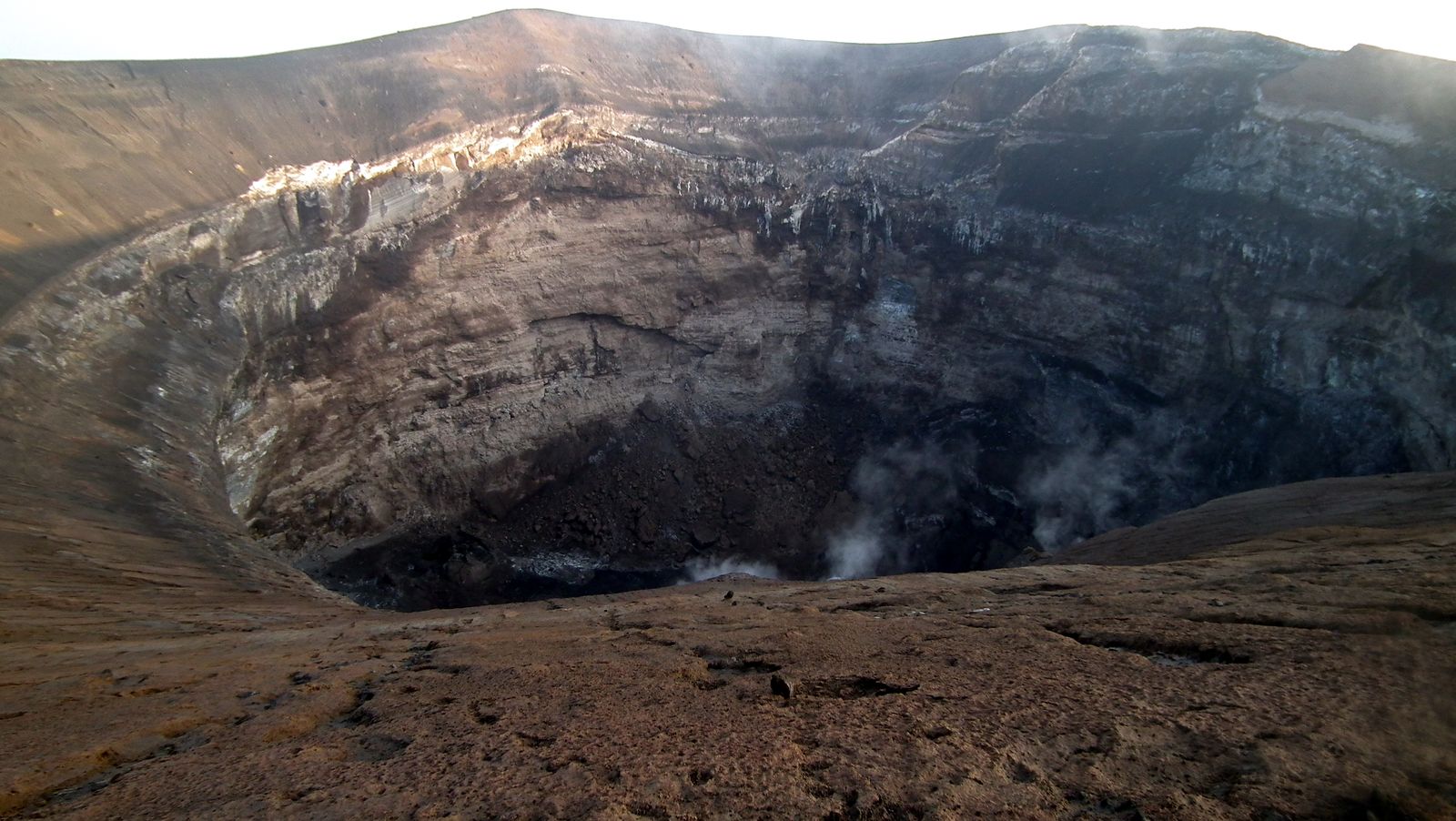 The deep summit crater of Ol Doinyo Lengai seen from the rim, with steam rising